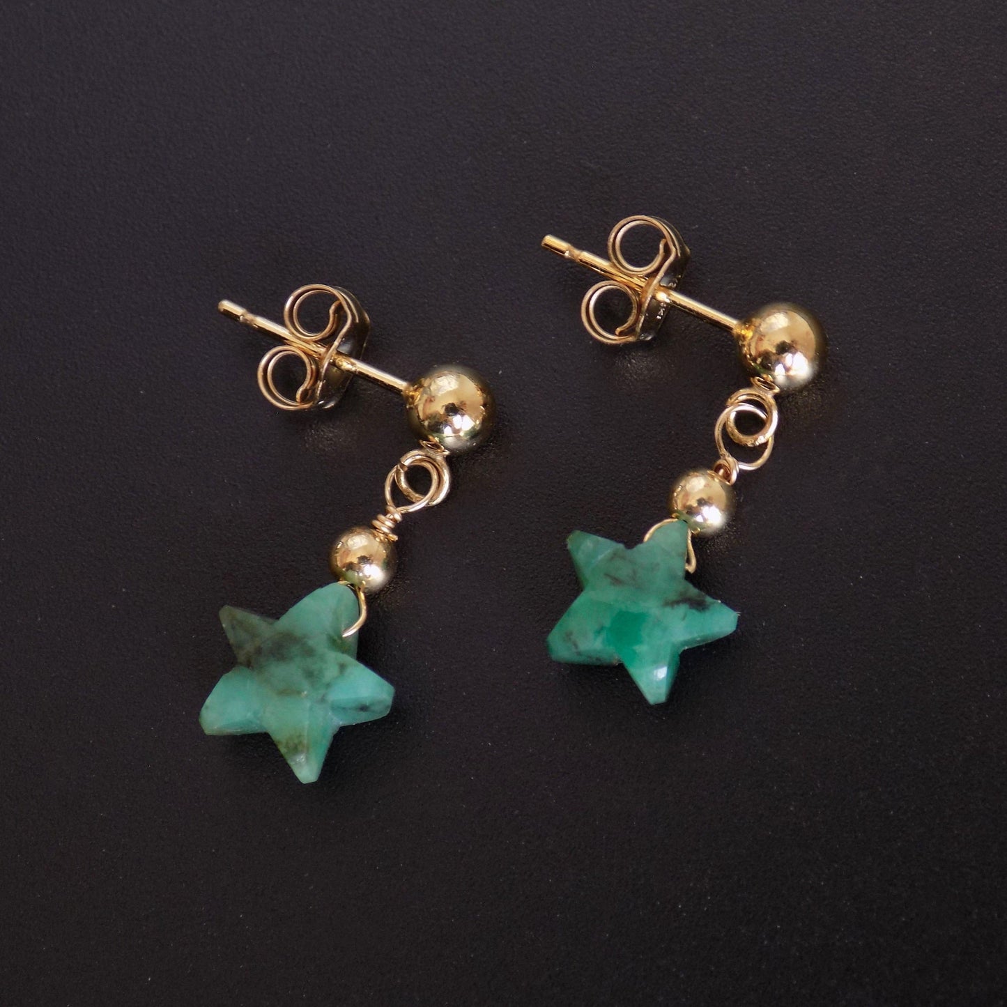 Dainty emerald star earrings on black background