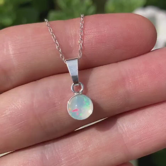 Video of dainty opal sterling silver pendant, with flowers in background