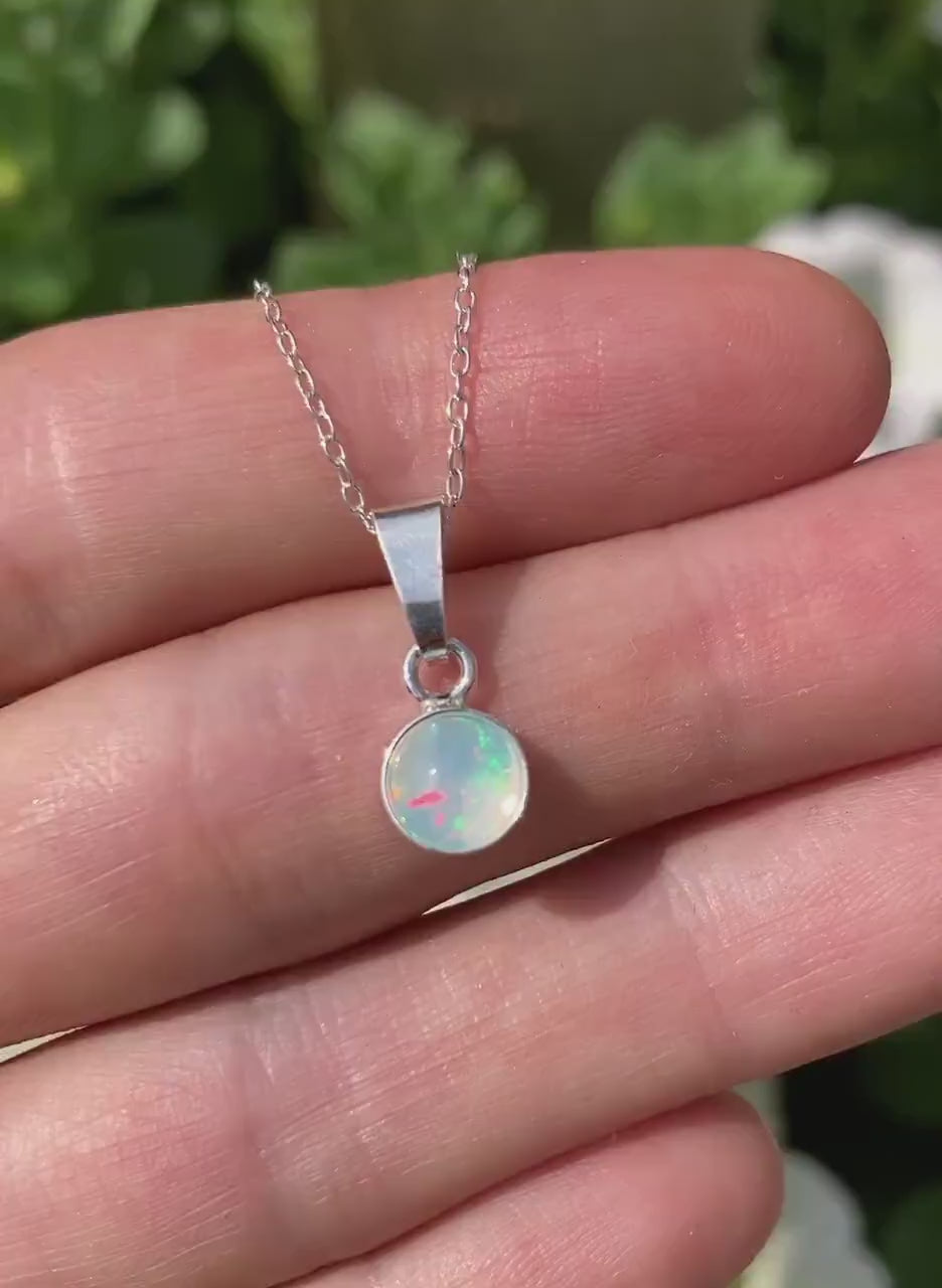 Video of dainty opal sterling silver pendant, with flowers in background